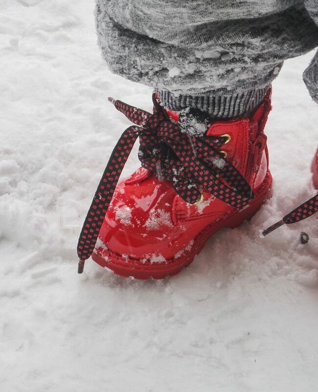 Dziecko w czerwonych butach stoi na śniegu
